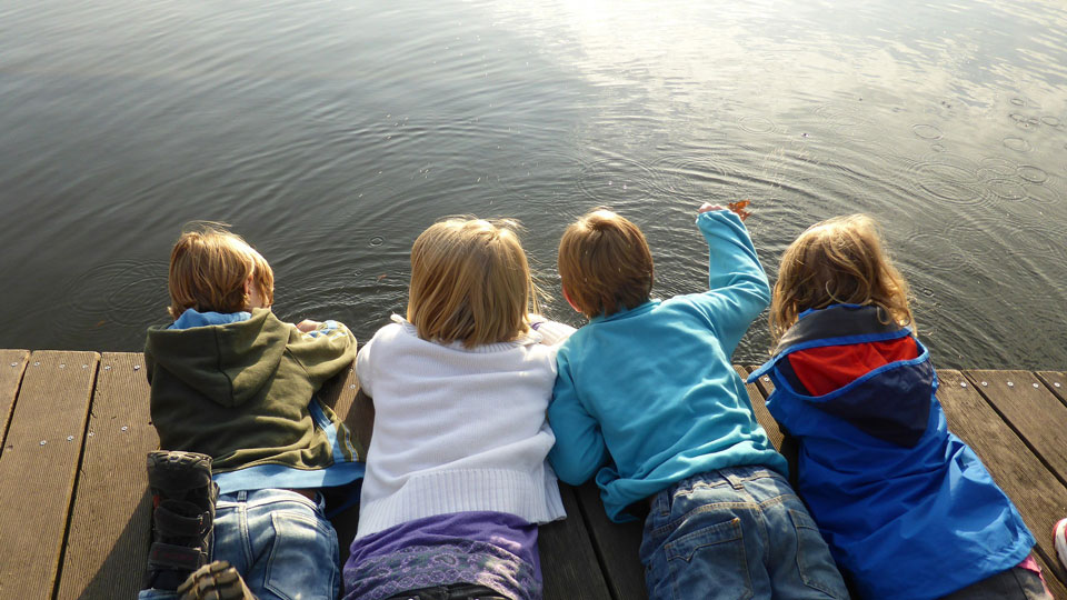 4 girls and boys lying prone on a jetty looking into the water