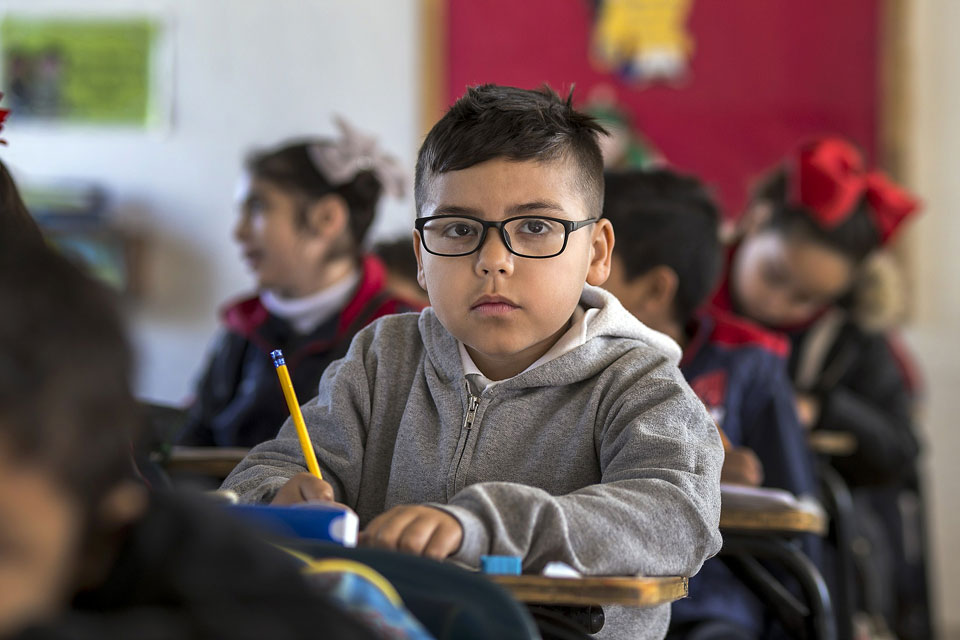 Boy writing with a pencil looking up in class
