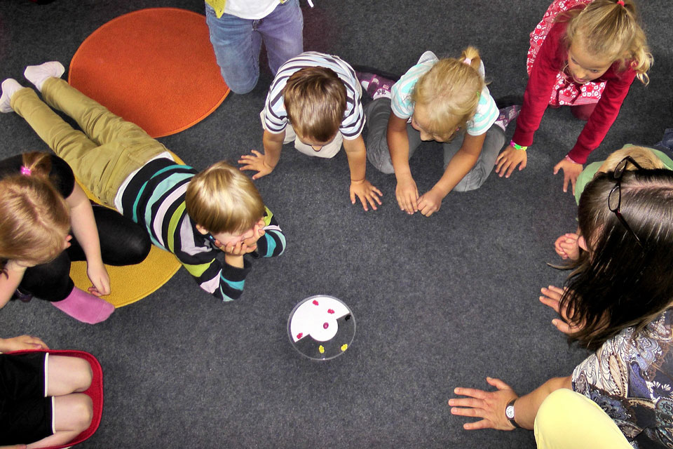 group of nursery age children gathered in a circle facing a dish with some sweets in it