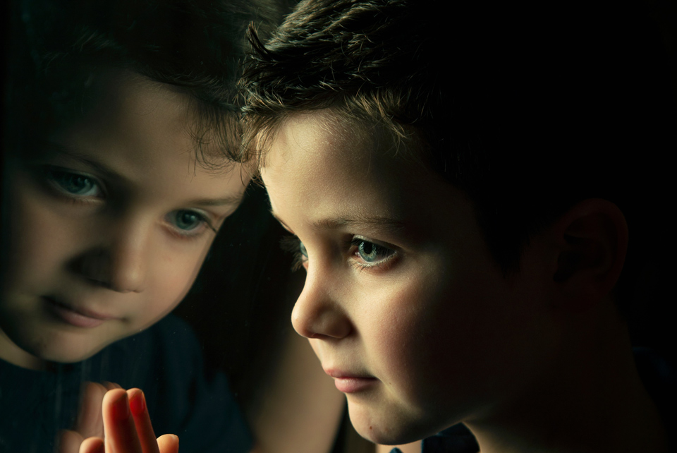 Child looking out of the window, with face reflected in the window
